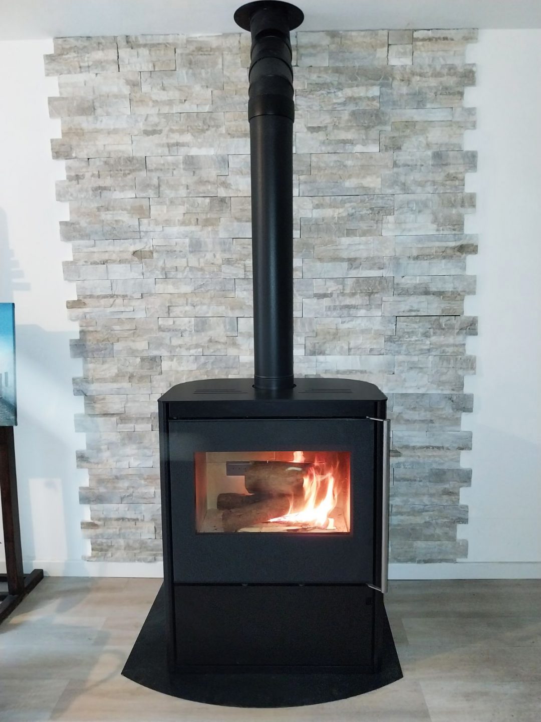 Poêle à bois Horizon de Morvan, avec une puissance de 8,1 kW, disponible en finitions acier noir et pierre de taille. Conçu pour des bûches de 50 cm, il intègre un espace de rangement pour le bois et offre une vue panoramique sur les flammes grâce à sa porte vitrée. Performant et écologique, ce modèle est certifié Flamme Verte pour un chauffage respectueux de l’environnement.