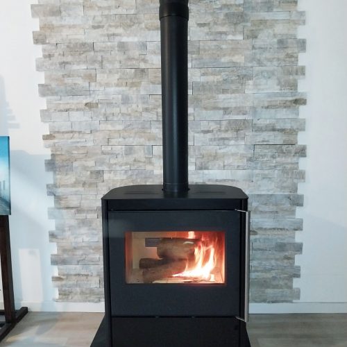Poêle à bois Horizon de Morvan, avec une puissance de 8,1 kW, disponible en finitions acier noir et pierre de taille. Conçu pour des bûches de 50 cm, il intègre un espace de rangement pour le bois et offre une vue panoramique sur les flammes grâce à sa porte vitrée. Performant et écologique, ce modèle est certifié Flamme Verte pour un chauffage respectueux de l’environnement.